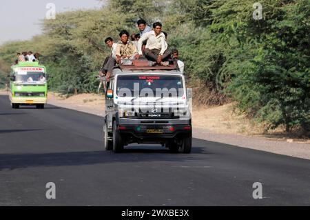 Several people sitting on the roof of an overloaded lorry driving on a country road, Jaipur, Rajasthan, India Stock Photo