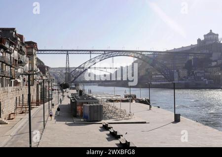 View of the Dom Luis I bridge over the Douro river, pedestrians strolling along a sunny river promenade with the bridge in the background, Porto Stock Photo