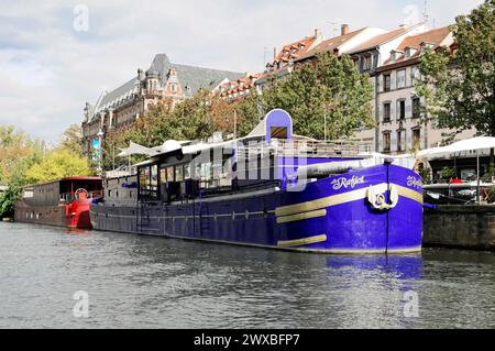 Boat trip on the L'ILL, Strasbourg, Alsace, residential boat moored on the banks of a river with a promenade and buildings in the background Stock Photo