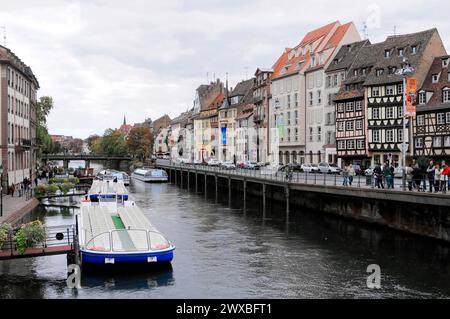 Boat trip on the L'ILL, Strasbourg, Alsace, riverbank with walkers, boats and traditional houses under a cloudy sky, Strasbourg, Alsace, France Stock Photo