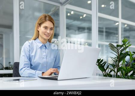 A focused professional woman engages with her laptop in a bright, contemporary office setting, embodying efficiency and dedication. Stock Photo