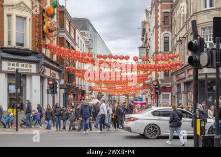 The hustle and bustle of people in Wardour street at the entrance to Chinatown, London. Watched over and greeted by the iconic Chinese Lion sculpture. Stock Photo
