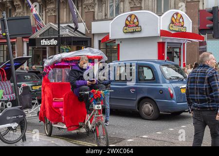 A pedicab or rickshaw rider looks at his phone while waiting for his next customer. The Pedicabs London Bill will regulate fares and enhance safety. Stock Photo