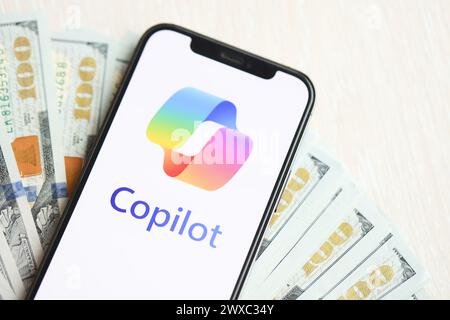 KYIV, UKRAINE - MARCH 17, 2024 Microsoft Copilot logo on iPhone display screen with many hundred dollar bills. Artificial Intelligence engine Stock Photo