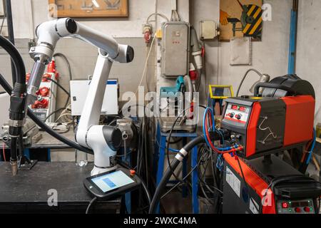 A modern welding robot in an old crowded welding workshop Stock Photo
