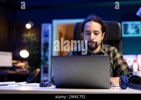 Young man typing email report on his laptop, researching and preparing presentations. Male university student working with paperwork research, browsing online website and finishing assignments. Stock Photo