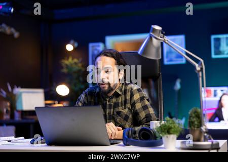 Bearded guy attends online training course at home, using laptop to work on new freelance contract. Self employed male student utilizing modern technology for his studies and research. Stock Photo