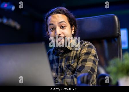 Creative writer, smiling and typing on laptop, passionately engaged in his work, combining technology and creativity. Cheerful man looking at device screen, checking emails and reviewing information. Stock Photo