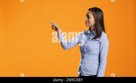 Filipino person checking holographic projection in studio, looking at modern hologram and working with artificial intelligence. Confident woman using metaverse technology reflection. Stock Photo