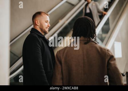 Two multiethnic business male people engaging in conversation on modern escalator. Stock Photo