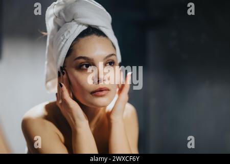 Young woman with a towel on her head checking her face in the mirror after a shower Stock Photo