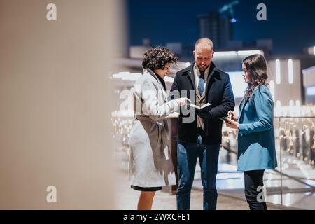 Three people sharing ideas on digital tablet at evening business event. Stock Photo