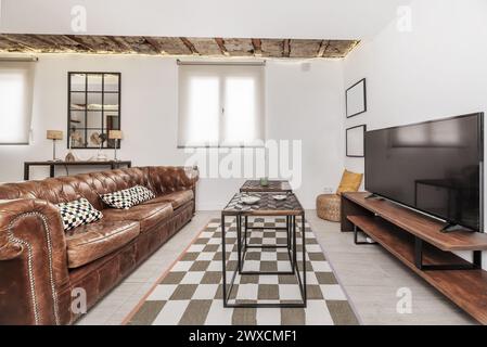 Living room with Chester model sofa bed upholstered in brown leather, industrial design wooden coffee table and sideboard with flat TV on top Stock Photo