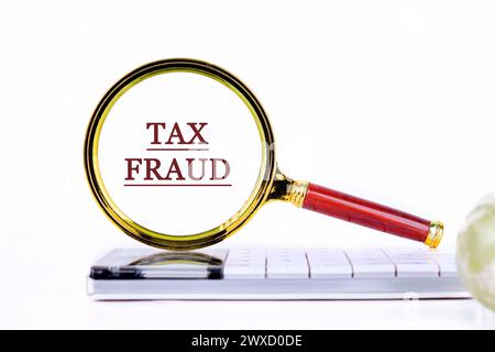 TAX FRAUD through a magnifying glass on a calculator on a light background Stock Photo