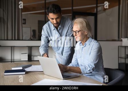 Two diverse younger and elder colleagues working together at laptop Stock Photo