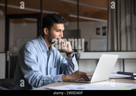 Pensive young Indian manager man working at laptop Stock Photo
