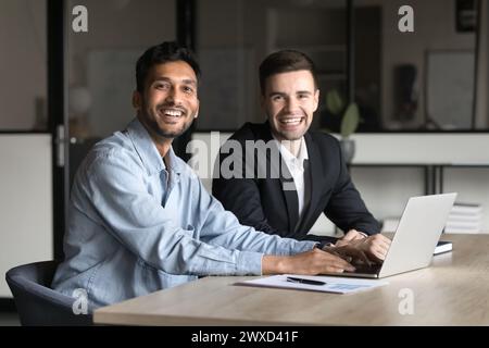 Two happy multiethnic business colleagues men sitting at workplace Stock Photo