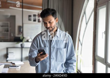 Positive focused Indian professional man typing on smartphone in office Stock Photo