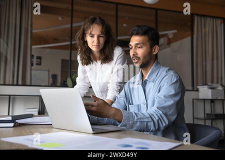 Two serious young Indian and Caucasian managers working at laptop Stock Photo