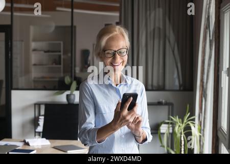 Happy successful mature businesswoman using professional application on smartphone Stock Photo