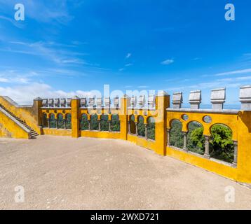 Wide view of the arched courtyard of Moorish-style arches of the Pena Palace, overlooking the clear blue sky and the Sintra mountain range. Portugal. Stock Photo