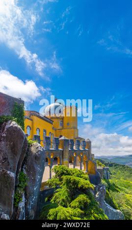 Exterior view of the arched courtyard of the Pena Palace, painted yellow, perched on large rocks with the Sintra mountain range in the background unde Stock Photo