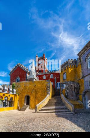 Wide view of the arched courtyard with stone stairs and the yellow and red painted walls of the Pena Palace, with a rock integrated into the facade. S Stock Photo