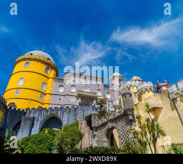 Exterior and wide view from the entrance path of the Pena Palace of yellow, red and mosaic colors. In Sintra under a sunny blue sky. Portugal. Stock Photo