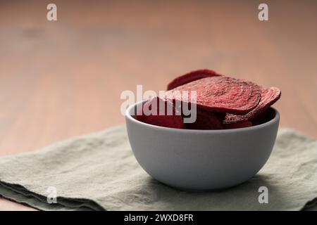 Beetroot chips in ceramic bowl on wooden table with linen napkin, shallow focus Stock Photo