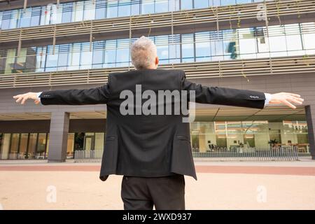 Rear view Happy businessman opens her arms in the air while walking outdoors. Stock Photo