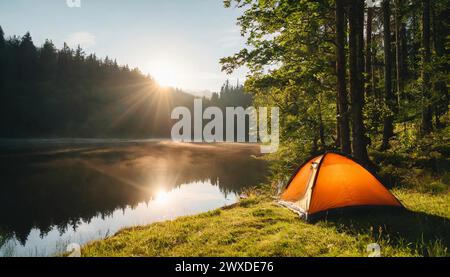 Camping waterproof tent on the shore of lake or river, green forest. Morning sun. Travel and tourism concept. Cinematic shot. Stock Photo