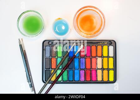 detail of Top view of Watercolors brushes and containers with water perfectly arranged on a white table. work utensils prepared to paint watercolors i Stock Photo