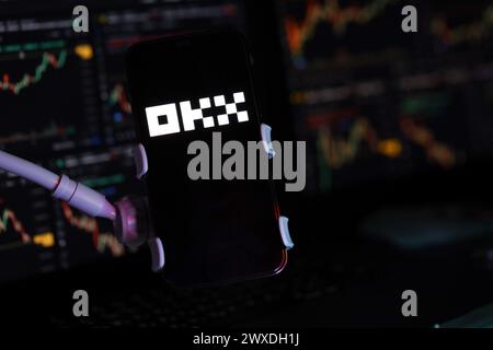 KYIV, UKRAINE - MARCH 15, 2024 OKX logo on iPhone display screen and crypto currency value charts. Cryptocurrency exchange portal Stock Photo