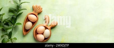 Two creative Easter wooden figured plates as bunny and carrot with Easter eggs of natural colors and green Ruskus twigs on textured green yellow backd Stock Photo