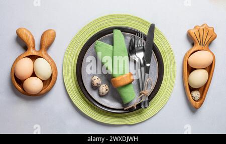 Easter table serving in trendy natural colors. Holiday table setting idea with round and wooden plates in form of bunny and carrot, green napkins, org Stock Photo