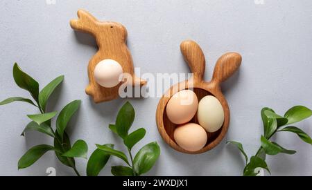 Organic Easter creative image. Eggs of natural colors in wooden figured plates in form of bunny and carrot and green Ruscus twigs on neutral gray back Stock Photo