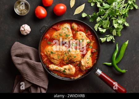 Georgian chicken stew with tomatoes and herbs (chakhokhbili) in cast iron skillet over dark stone background. Baked chicken with tomato vegetable grav Stock Photo