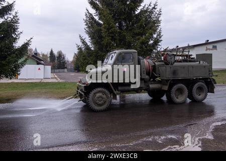 A large green truck is spraying water on the road. The truck is parked in front of a building with a red letter A on it Stock Photo