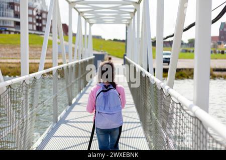 Rear view of a young woman walking on a bridge over a river Stock Photo