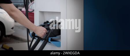 Hand holding EV charging plug in front of camera with blurred background of outdoor. Driver of electric car hold batteries charger plug. Sustainable e Stock Photo