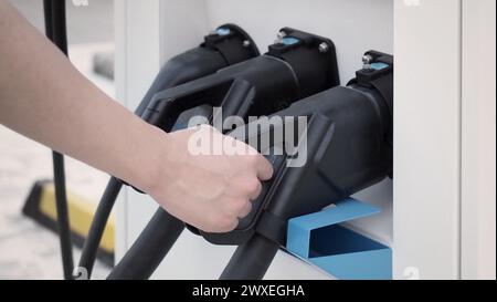 Hand holding EV charging plug in front of camera with blurred background of outdoor. Driver of electric car hold batteries charger plug. Sustainable e Stock Photo