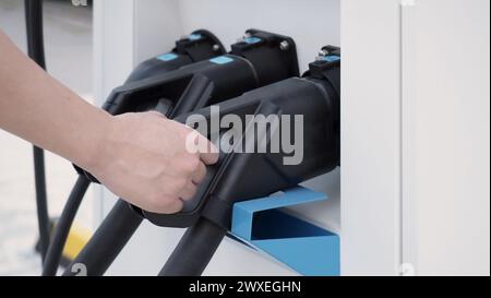 Hand holding EV charging plug in front of camera with blurred background of outdoor. Driver of electric car hold batteries charger plug. Sustainable e Stock Photo
