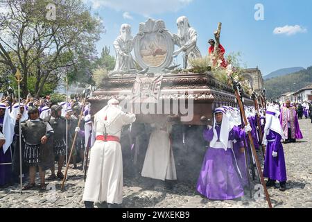 Antigua, Guatemala. 29th Mar, 2024. Catholic penitents pause the massive La Merced Good Friday processional float as they pass the Cathedral San Jose during Semana Santa, March 29, 2024 in Antigua, Guatemala. The opulent processions, detailed alfombras and centuries-old traditions attract more than 1 million people to the ancient capital city. Credit: Richard Ellis/Richard Ellis/Alamy Live News Stock Photo