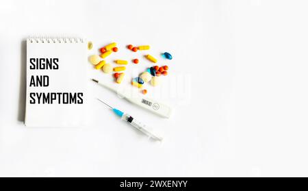 On a white background, a thermometer, pills and a notepad with the text SIGNS AND SYMPTOMS. Medical concept Stock Photo