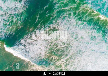 aerial view of the foam of waves breaking near the beach, turquoise sea seen from a drone. Stock Photo