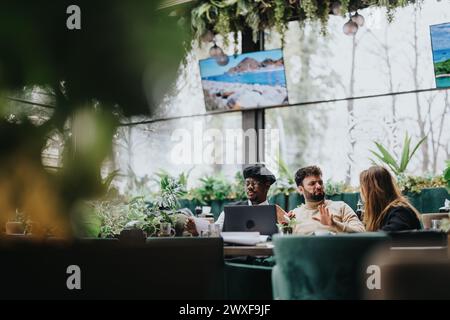 Multiethnic business team having a collaborative meeting in a plant-filled restaurant, illustrating a casual yet productive workplace atmosphere. Stock Photo