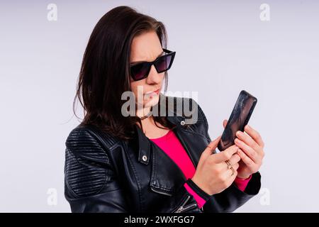A frustrated young woman with a broken phone in her hands. White isolated background. Broken Gadget Stock Photo