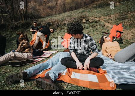 Friends enjoying a picnic with a guitar on a striped blanket outdoors. Stock Photo