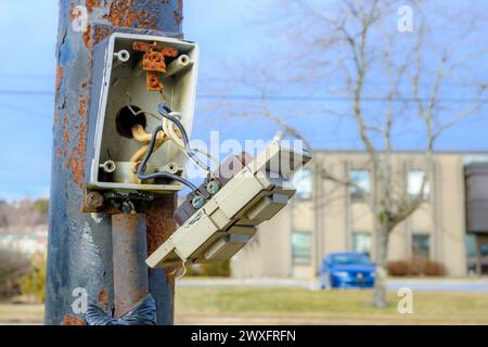 A broken electrical panel on the side of an outdoor pole. The front is hanging off, held to the box only by exposed wires. Closeup view. Stock Photo