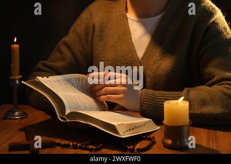 Woman reading Bible at table with burning candles, closeup Stock Photo